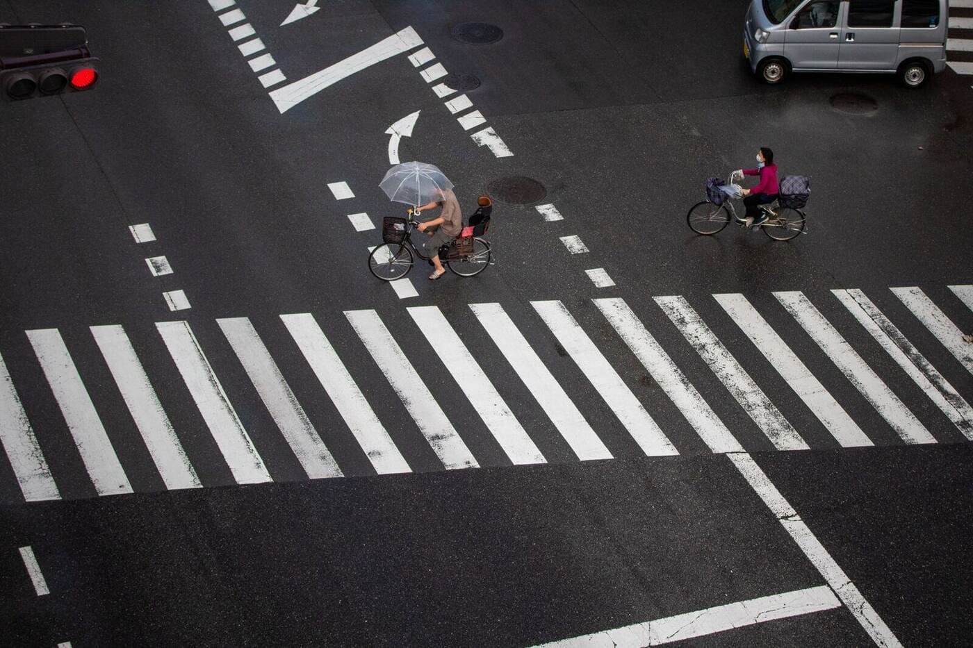Cyclists navigate a rainy city crosswalk with umbrellas for protection.